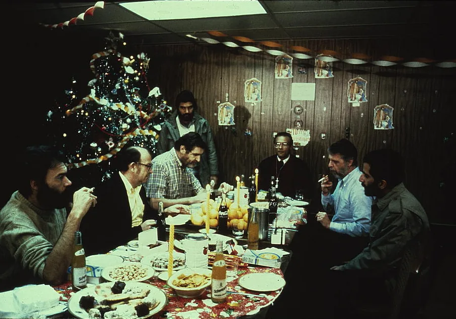 American hostages seated at a long table for a holiday meal inside the embassy in Tehran, with a Christmas tree behind them