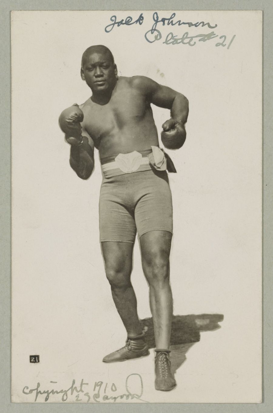 Jack Johnson standing in boxing trunks and gloves, full length portrait.