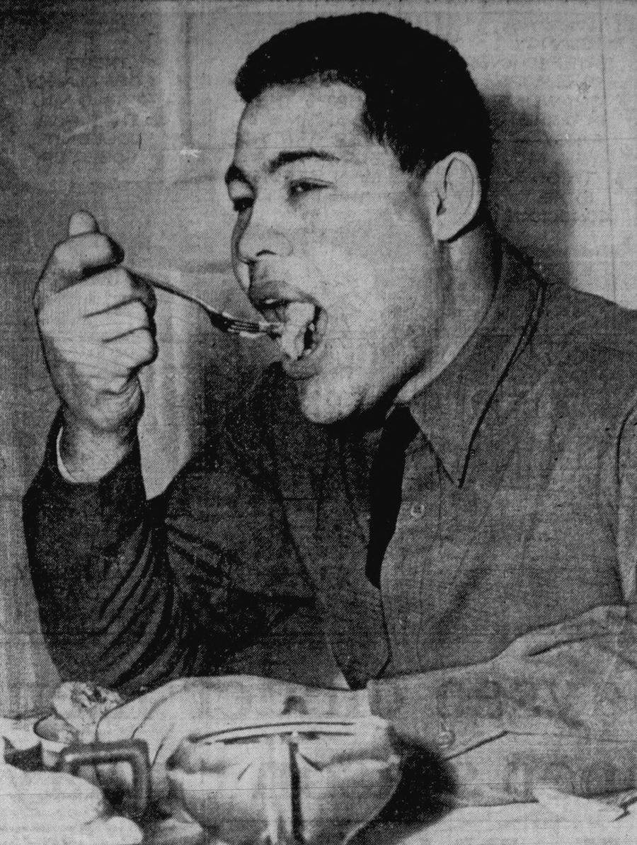 Joe Louis in an Army uniform eating from a spoon at a mess hall table.