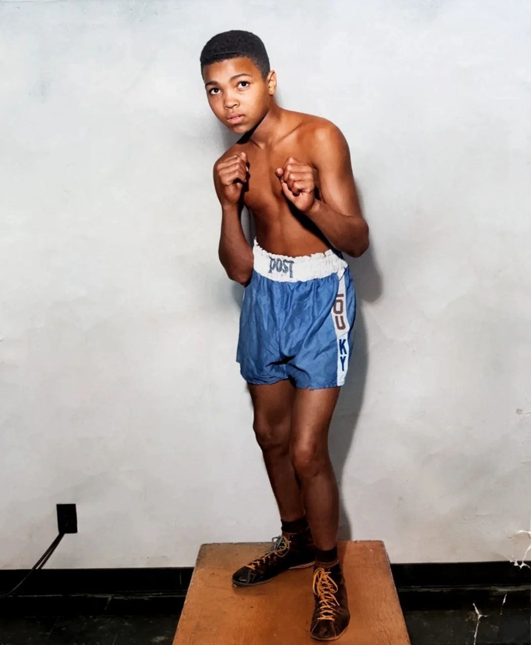Cassius Clay as a boy in boxing stance, wearing Louisville trunks.