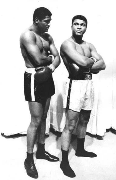 Muhammad Ali and Ernie Terrell standing side by side in boxing trunks and gloves.