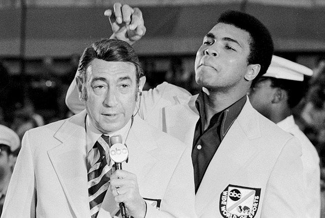 Muhammad Ali reaching over to lift Howard Cosell's hairpiece while Cosell speaks into an ABC microphone.