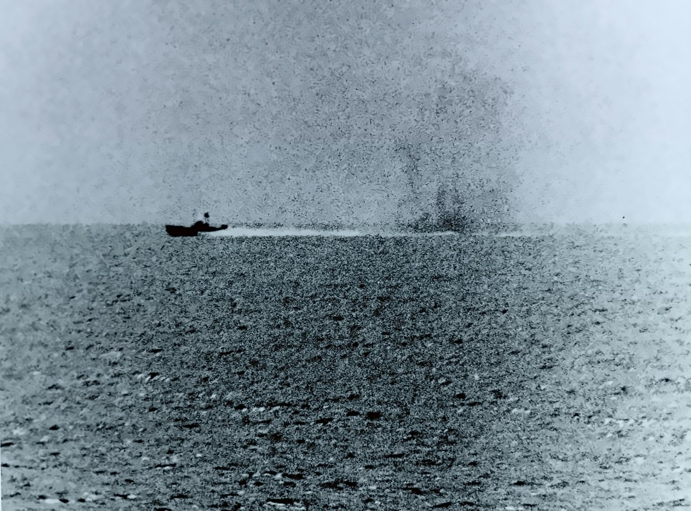 A torpedo boat on the horizon with a column of smoke and spray rising behind it.
