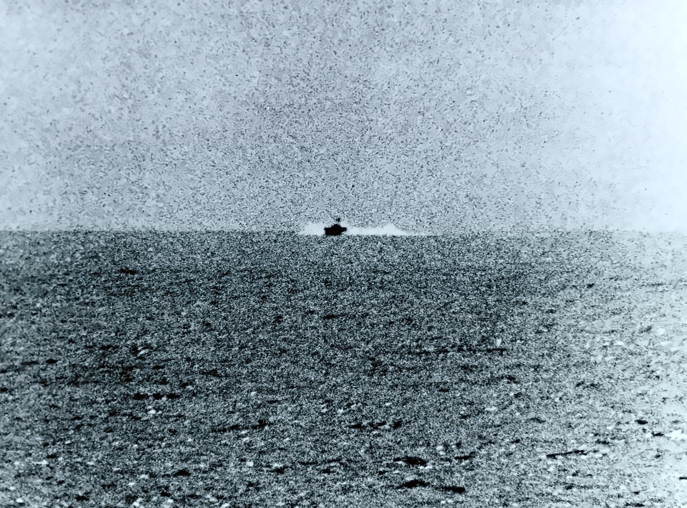 A small North Vietnamese torpedo boat running across flat gray sea toward the camera's left.