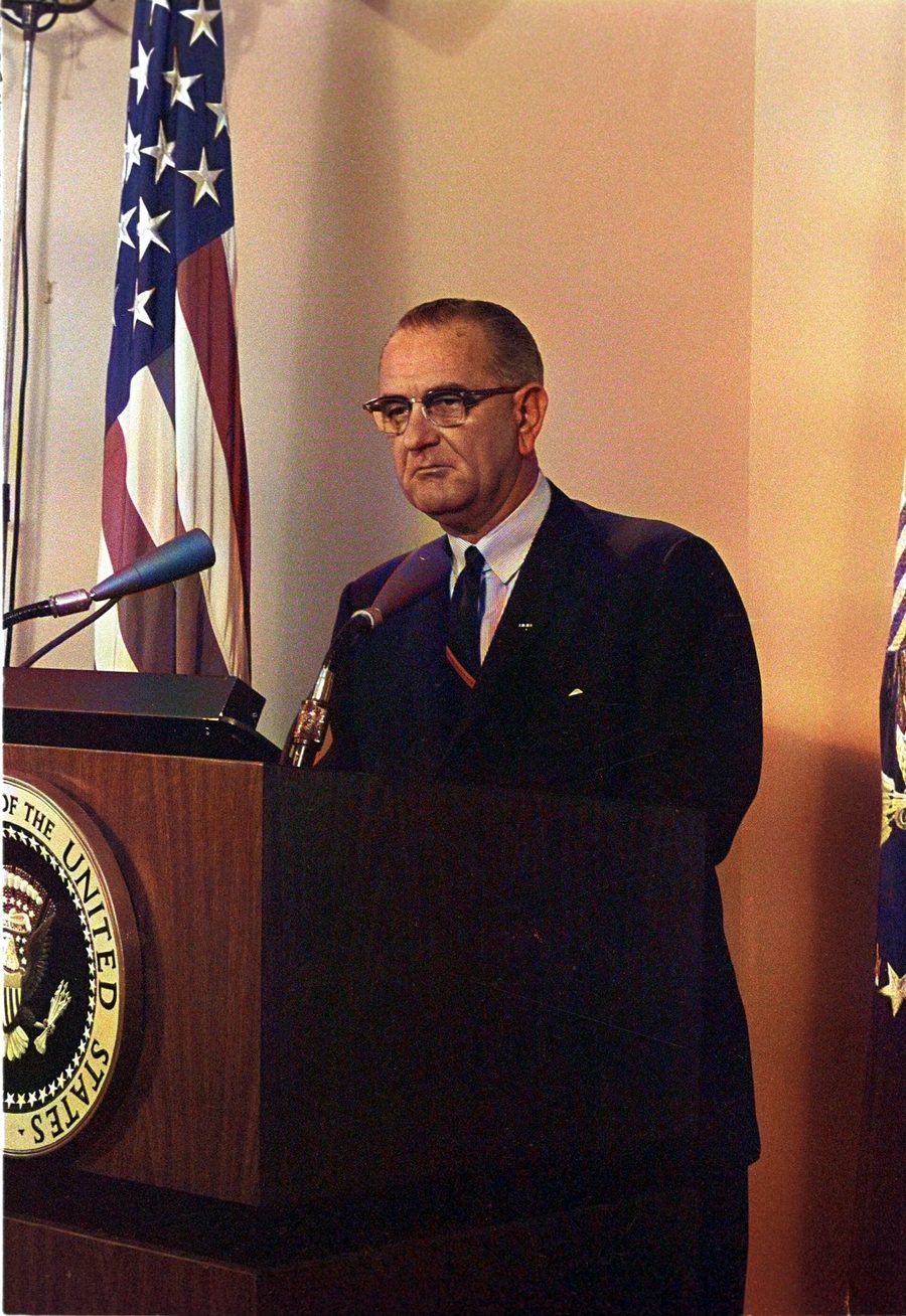 President Johnson standing at a lectern with the presidential seal, an American flag behind him.