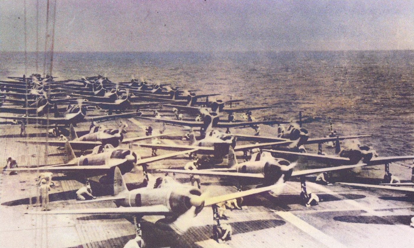 Rows of Japanese warplanes parked on the flight deck of an aircraft carrier with open ocean behind.