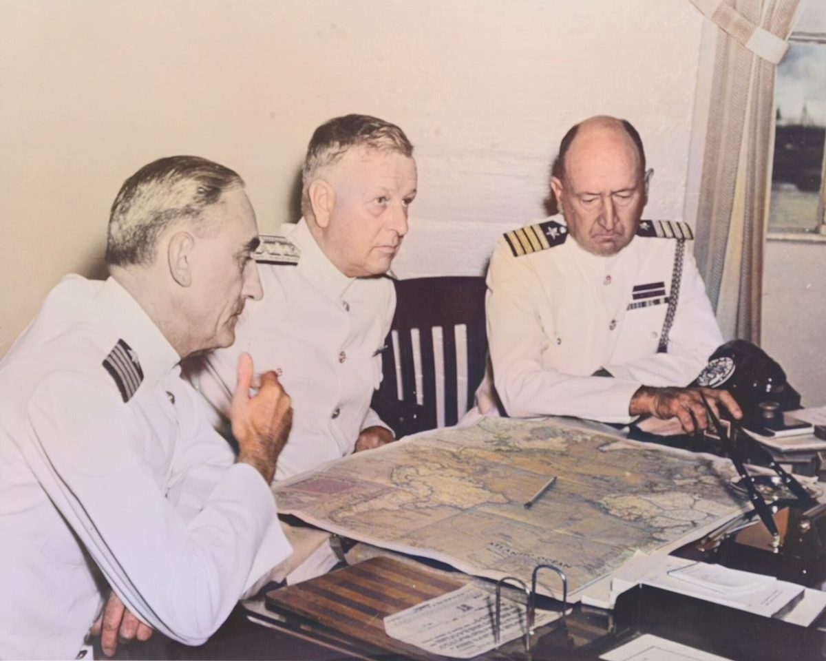 Admiral Kimmel and two senior officers in white uniforms leaning over a chart spread on a desk.