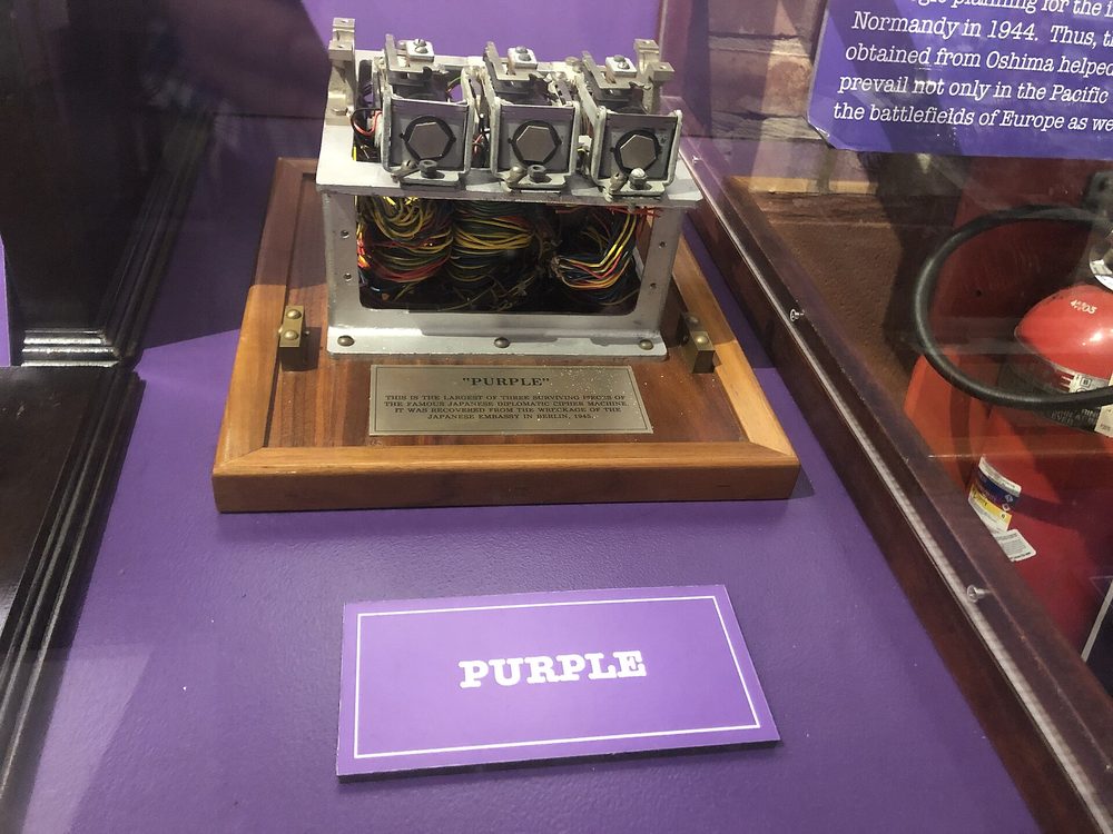 A metal fragment of a Japanese Purple cipher machine with rows of switches and colored wires, displayed in a museum case.