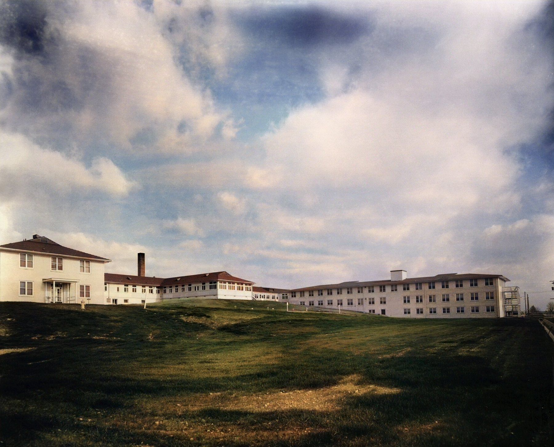 Colorized photograph of the long white wooden buildings of the Oak Ridge Army hospital under a cloudy sky in 1944