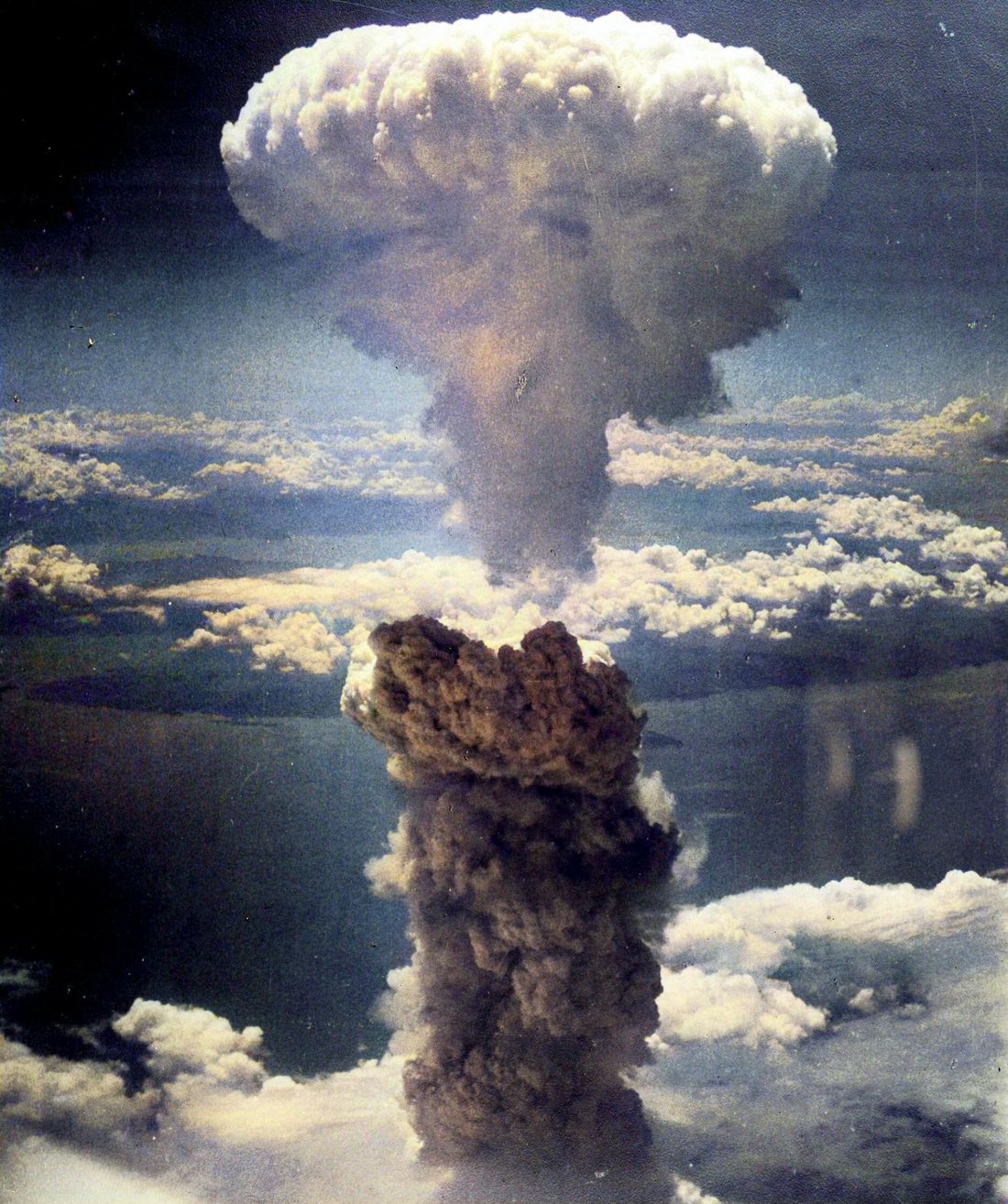 A towering mushroom cloud rises high above a layer of white clouds.