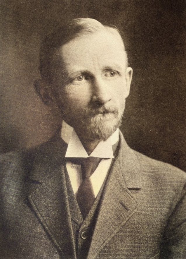 Portrait of a bearded man in a dark suit and high collar.