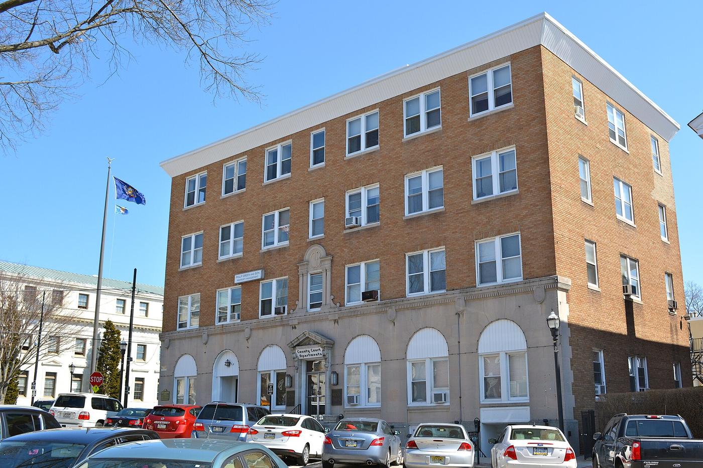 A four story brick building at One Veterans Square in Media, Pennsylvania, with the white county courthouse at left.