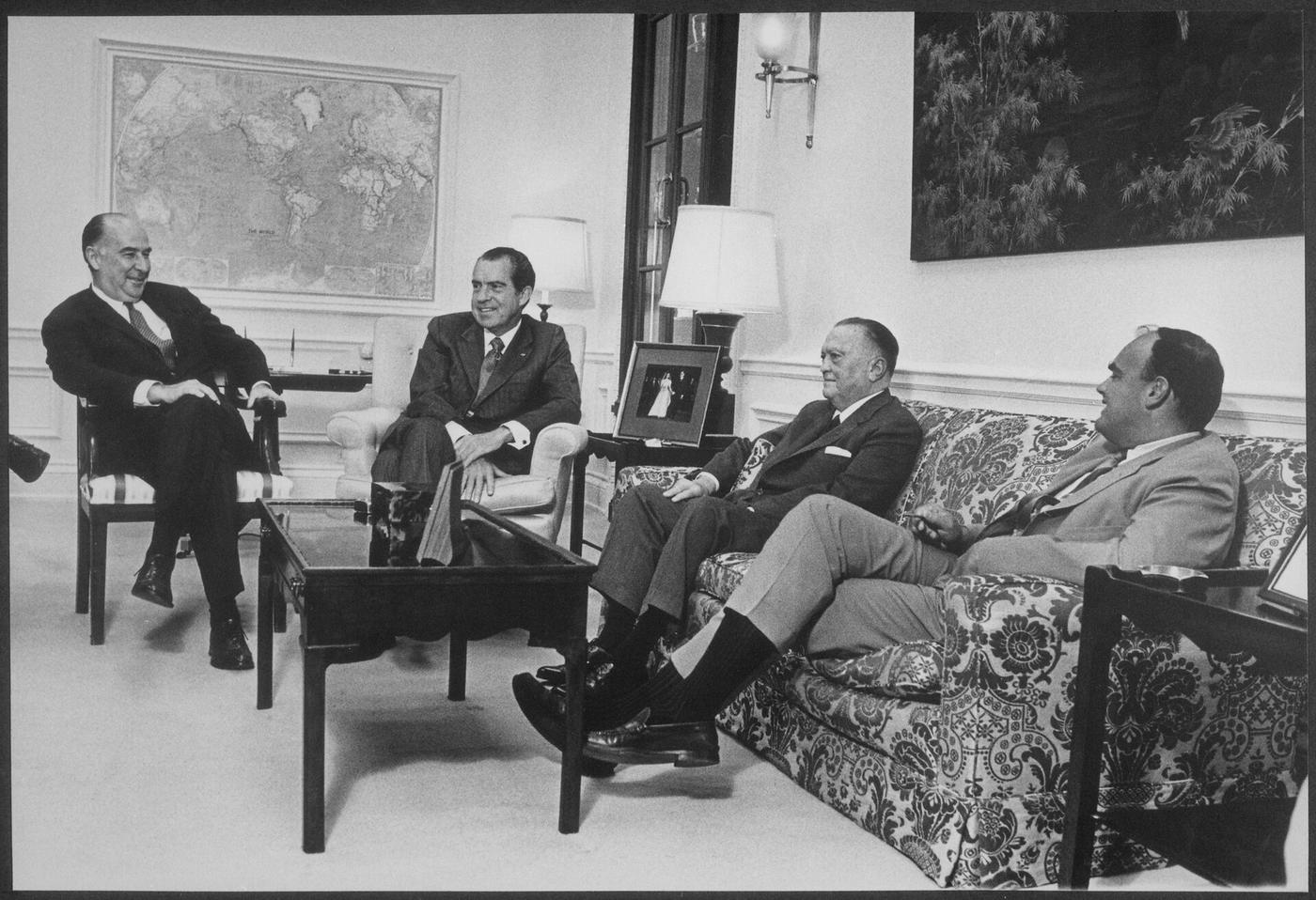 Four men in suits talking in a living room at the White House.