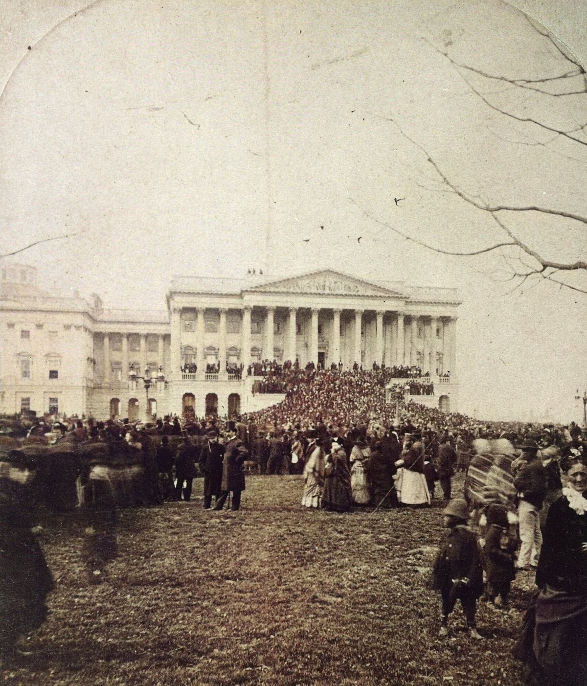 Colorized photograph of a crowd on a lawn before the columned Senate wing of the Capitol under bare winter trees