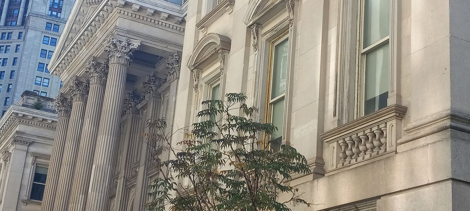 The marble front of the Tweed Courthouse with tall columns, seen from street level.