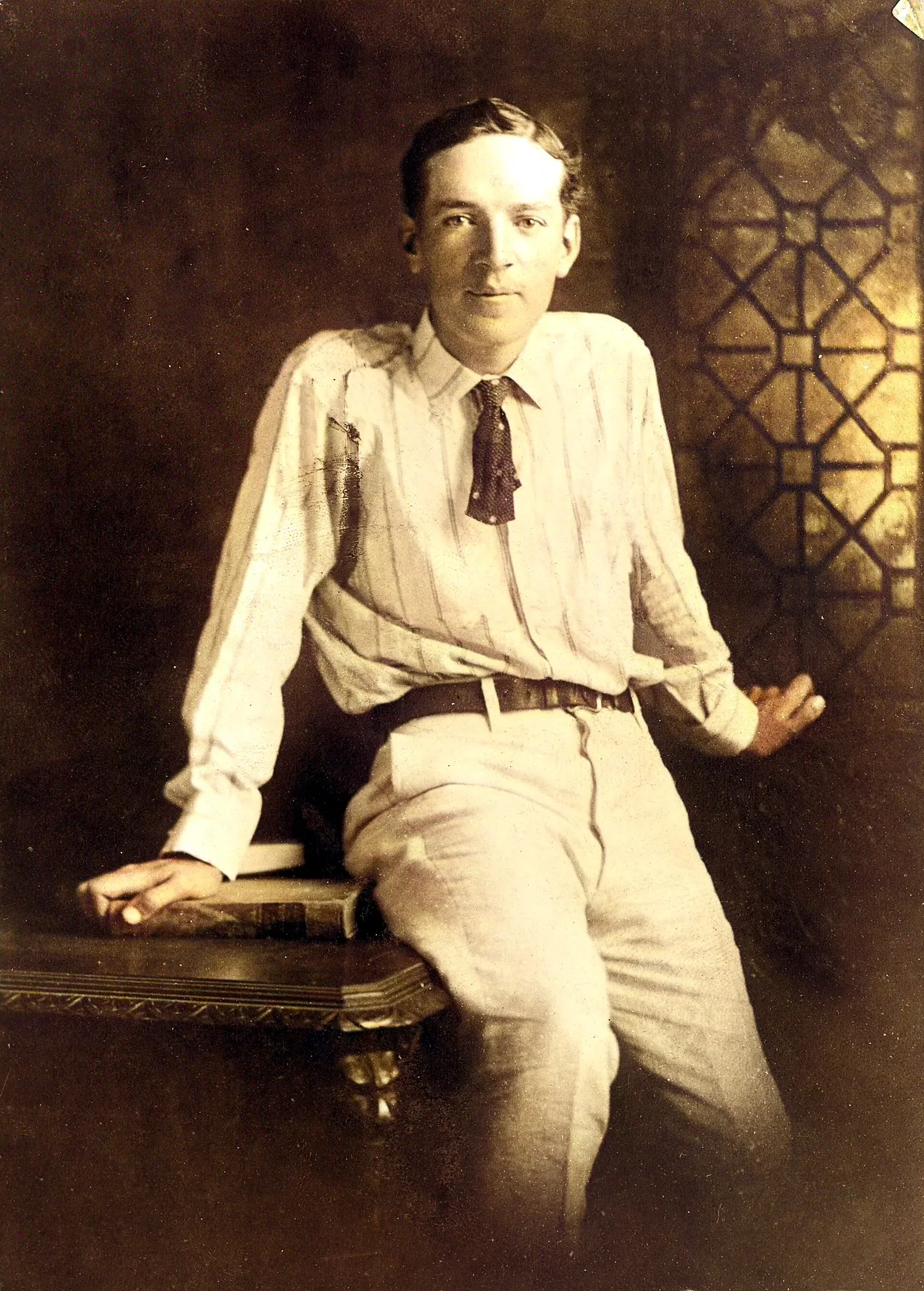 Young Upton Sinclair seated on the edge of a table in a white shirt and tie
