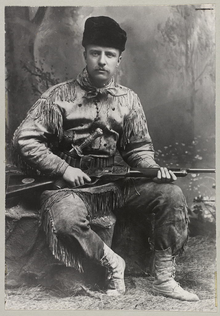 Young adult Roosevelt wearing ranching clothes, posed with a rifle.