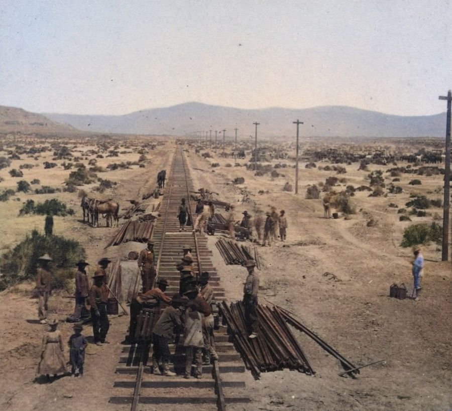 Workers unloading rails at the end of the track on a flat desert plain.