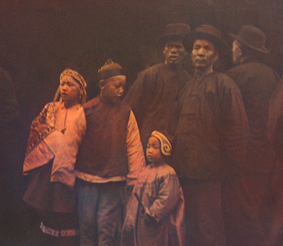 A group of Chinese men and children in traditional clothing standing together on a street.
