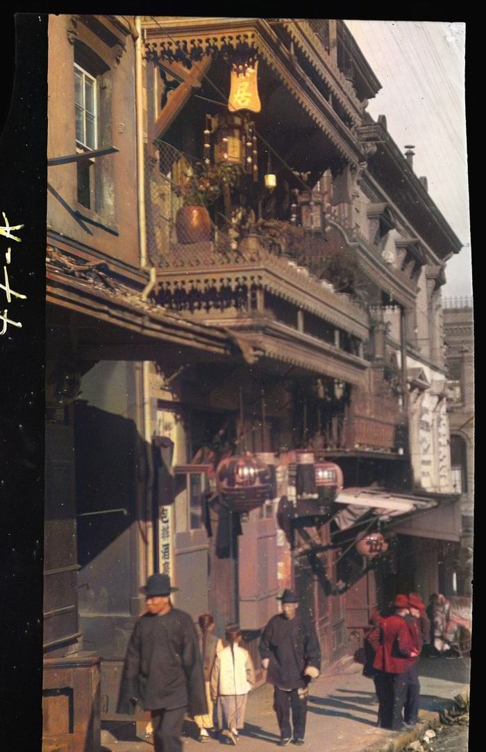 A narrow street in San Francisco's Chinatown with painted balconies and lanterns above people walking.